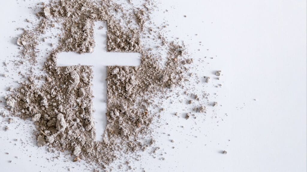 A cross cut out of sand on top of white background.