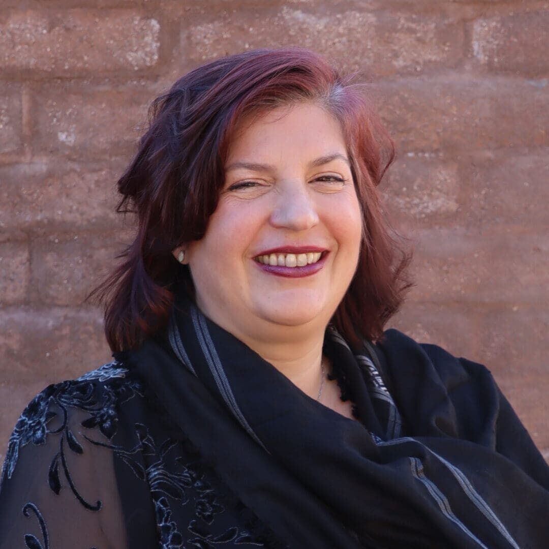 A woman with red hair and black dress smiling.